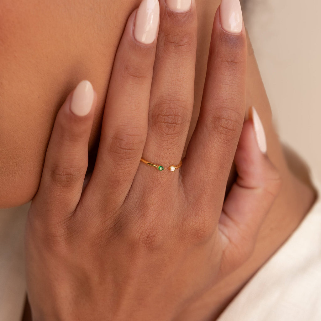Close-up of a hand with nude nail polish wearing the Duo Birthstone & Opal Ring, featuring a small green birthstone and an opal.