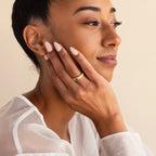 A woman with manicured nails smiles softly, resting her hand on her face and wearing the Ribbed Birthstone Signet Ring.