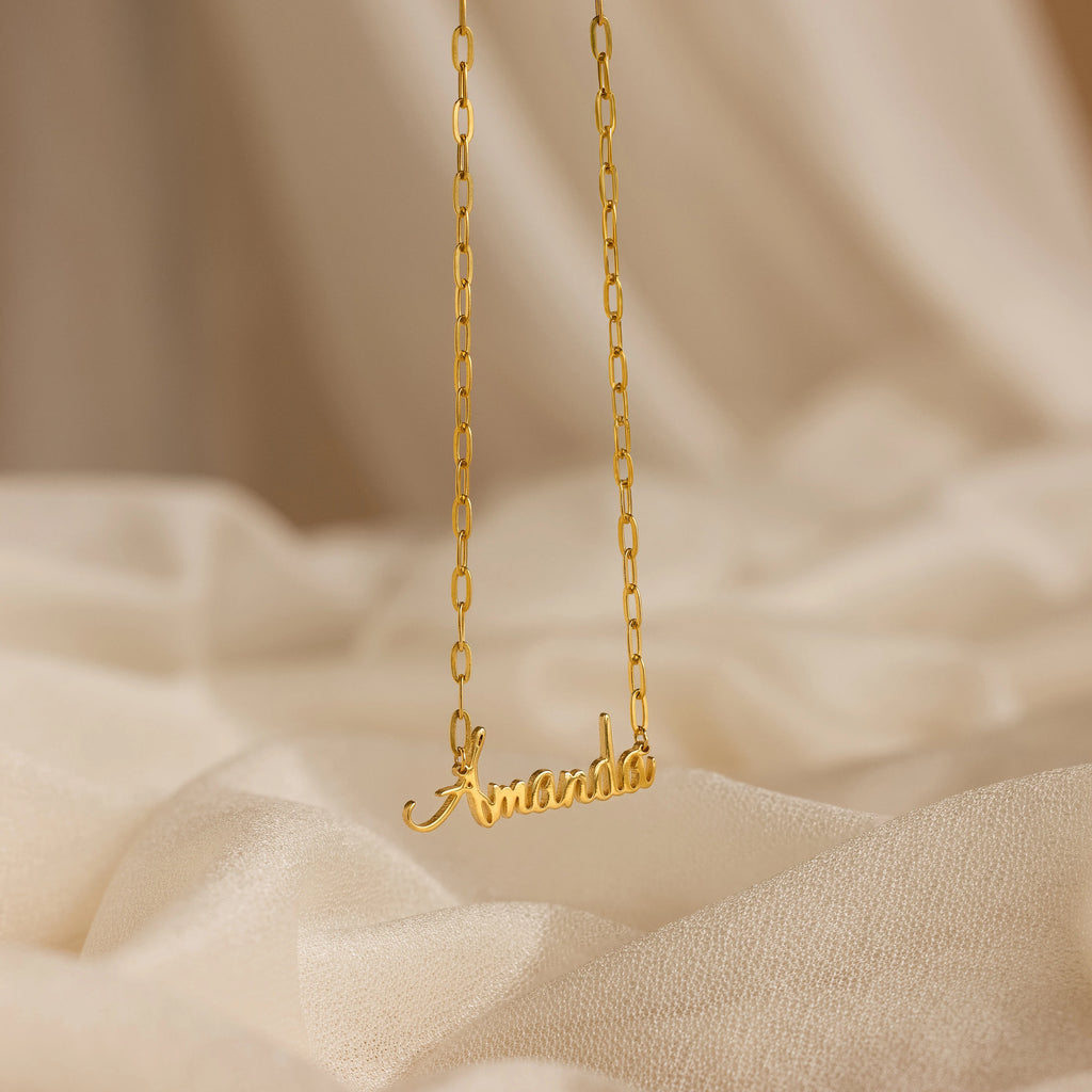 Luna Name Necklace in Paperclip Chain, personalized with "Amanda," shown on a soft beige fabric background.