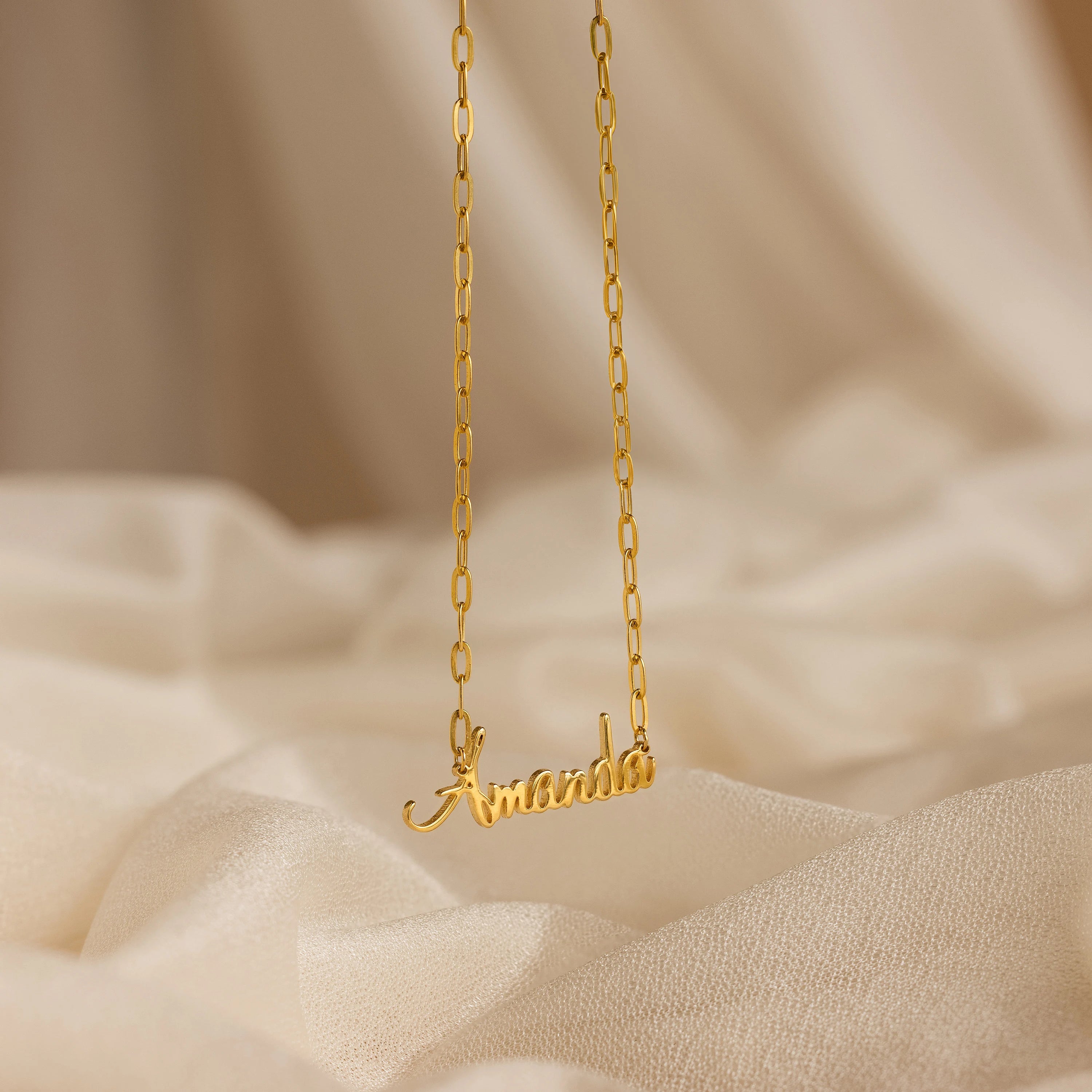 Luna Name Necklace in Paperclip Chain, personalized with "Amanda," shown on a soft beige fabric background.
