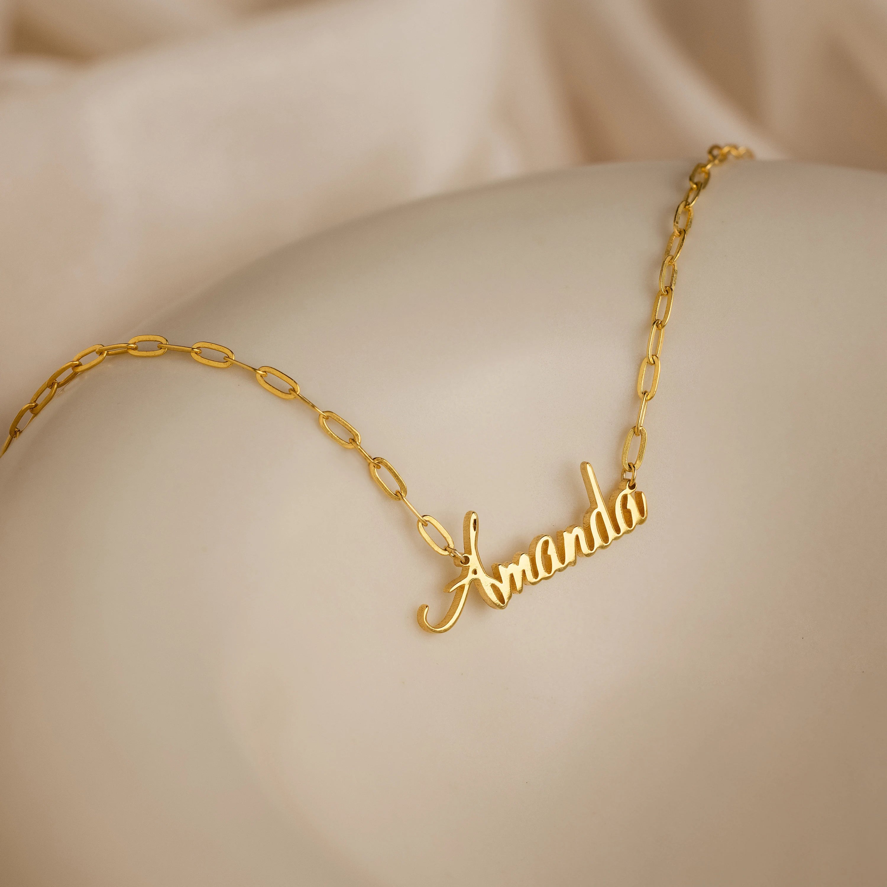 Luna Name Necklace in Paperclip Chain, personalized with "Amanda" in elegant cursive, is displayed on a smooth beige surface.