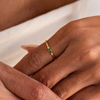 A hand wears the Marquise Bezel Birthstone Ring on the ring finger, showcasing a green gemstone and a small clear stone.