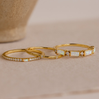 The Pave Opal Ring Set features four delicate gold rings with opal and diamond accents, artfully displayed on a neutral surface for a timeless look.