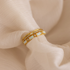The Pave Opal Ring Set, featuring opal and diamond accents in a classic gold design, rests on soft, light beige fabric.