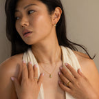 Woman with long dark hair wearing a cream sleeveless top and gold jewelry, including the Oval Labradorite Pendant Necklace, gazes to the side.