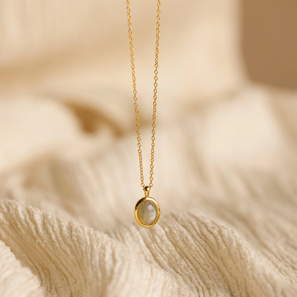 Oval Labradorite Pendant Necklace shown on a soft, cream-colored textured fabric background.
