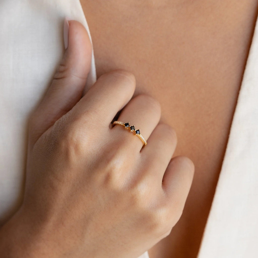 A hand wears a delicate gold ring with black and white stones, perfect for layering or pairing with your favorite Black Diamond Rings Set, shown against a cream blouse.
