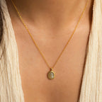 An Oval Labradorite Pendant Necklace rests on a person in a cream V-neck top.