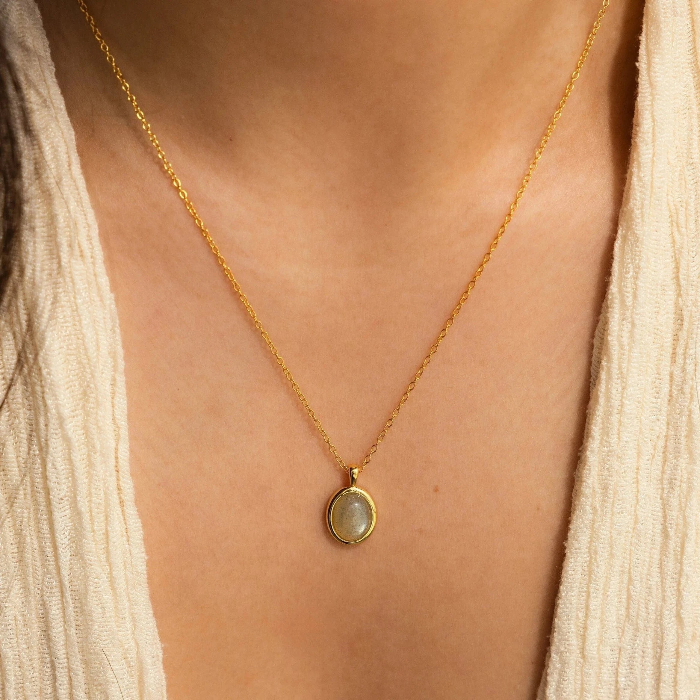 An Oval Labradorite Pendant Necklace rests on a person in a cream V-neck top.