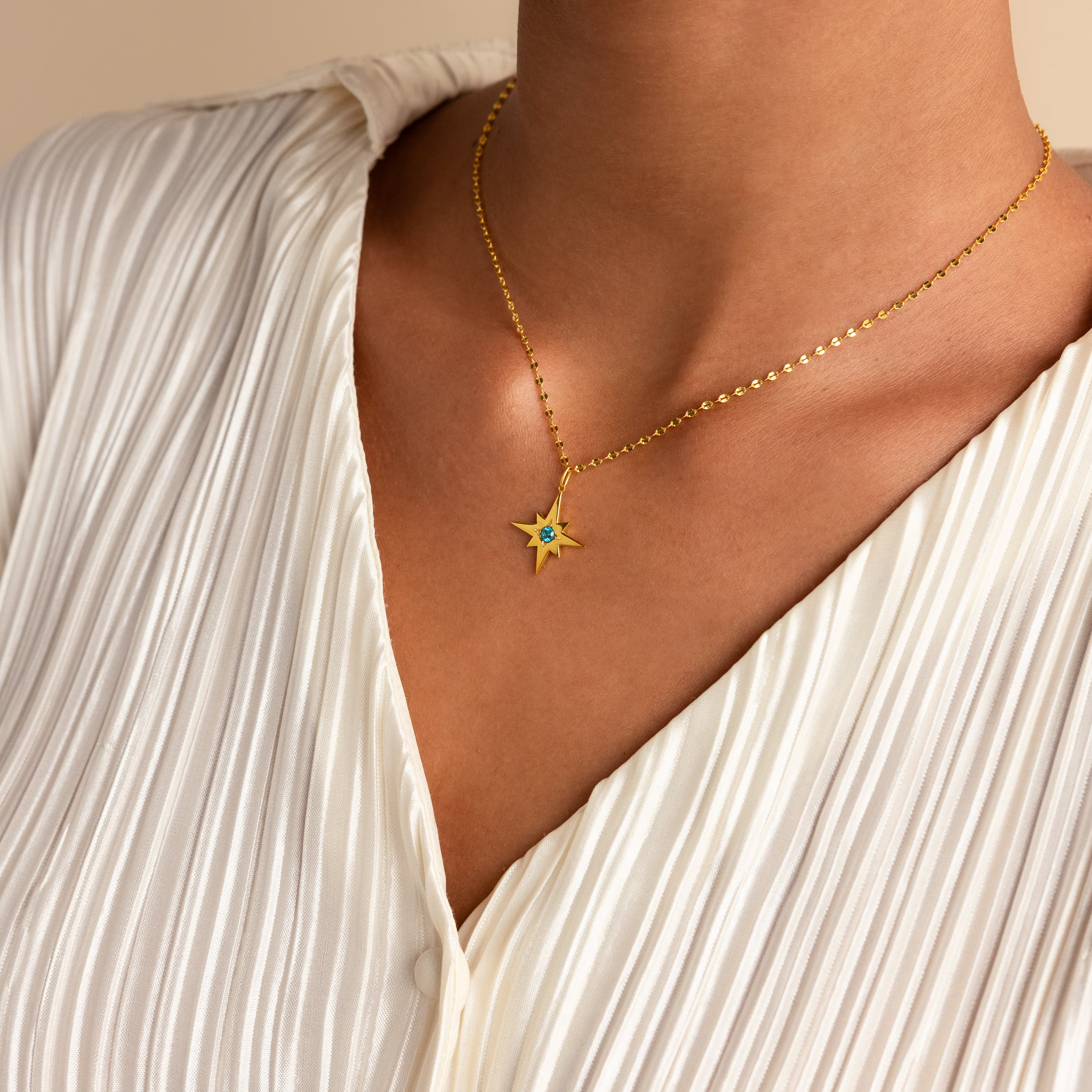 A person wearing the Star Birthstone Necklace, a gold celestial pendant, over a white pleated blouse.