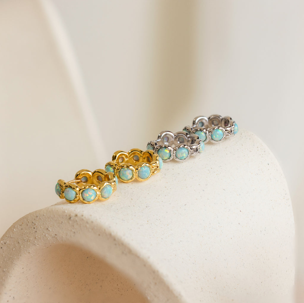 Gold and silver gemstone rings are arranged on a textured surface with Opal Bezel Huggies and beaded hoops, creating a timeless, curated look.