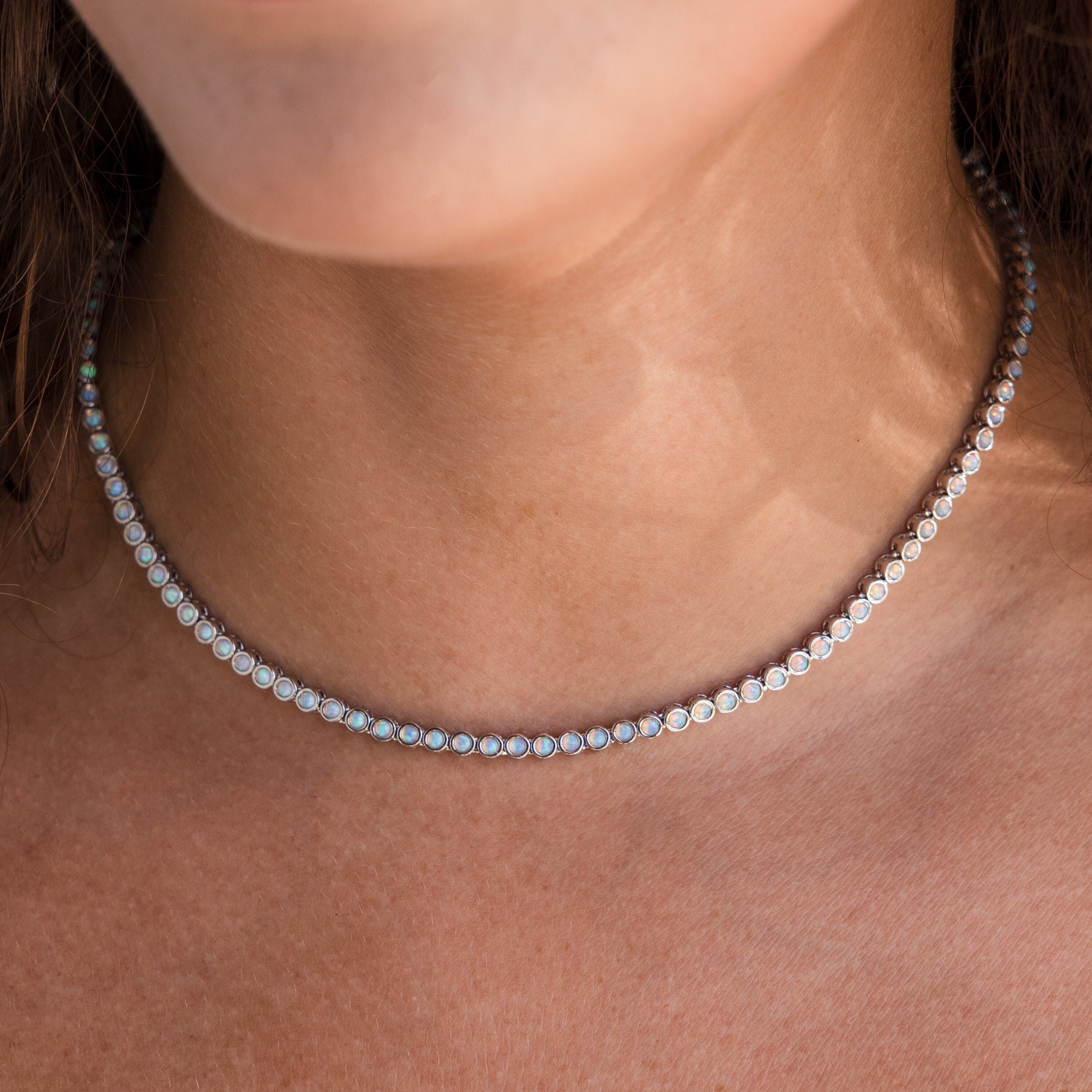A close-up of a woman's neck wearing the Opal Bezel Tennis Necklace, highlighting the necklace's elegant opal accents and iridescent charm.