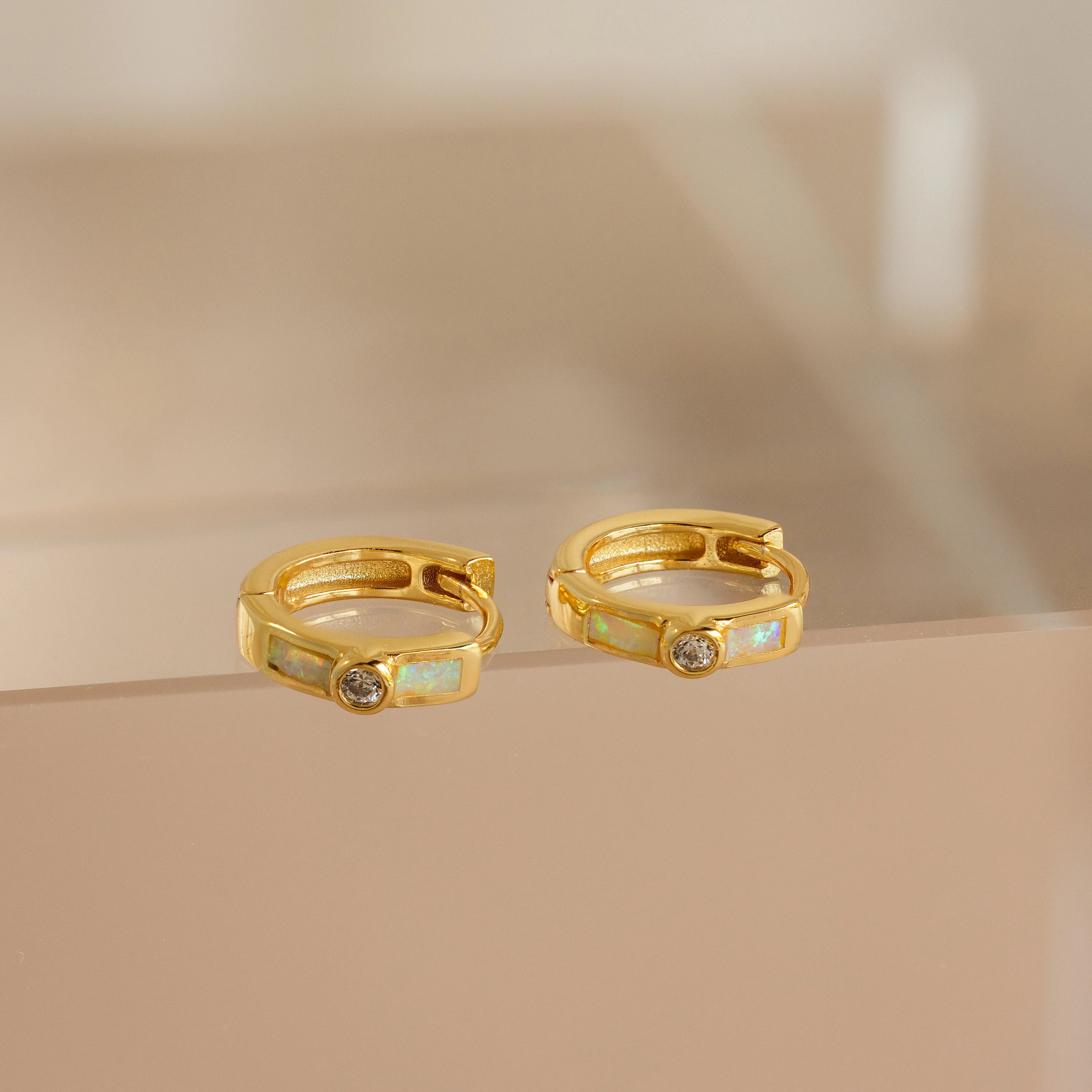 Opal Inlay Diamond Huggies: Elegant gold hoop earrings with opal inlay and a small round diamond, displayed on a beige surface.