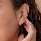 A hand touches a small Opal Inlay Diamond Huggie earring worn on a woman with wavy brown hair, highlighting the earring’s elegant, subtle shine.