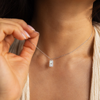 A woman holds the Pave Pearl North Star Necklace with its rectangular pendant near her neck, highlighting the celestial elegance of this jewelry piece.