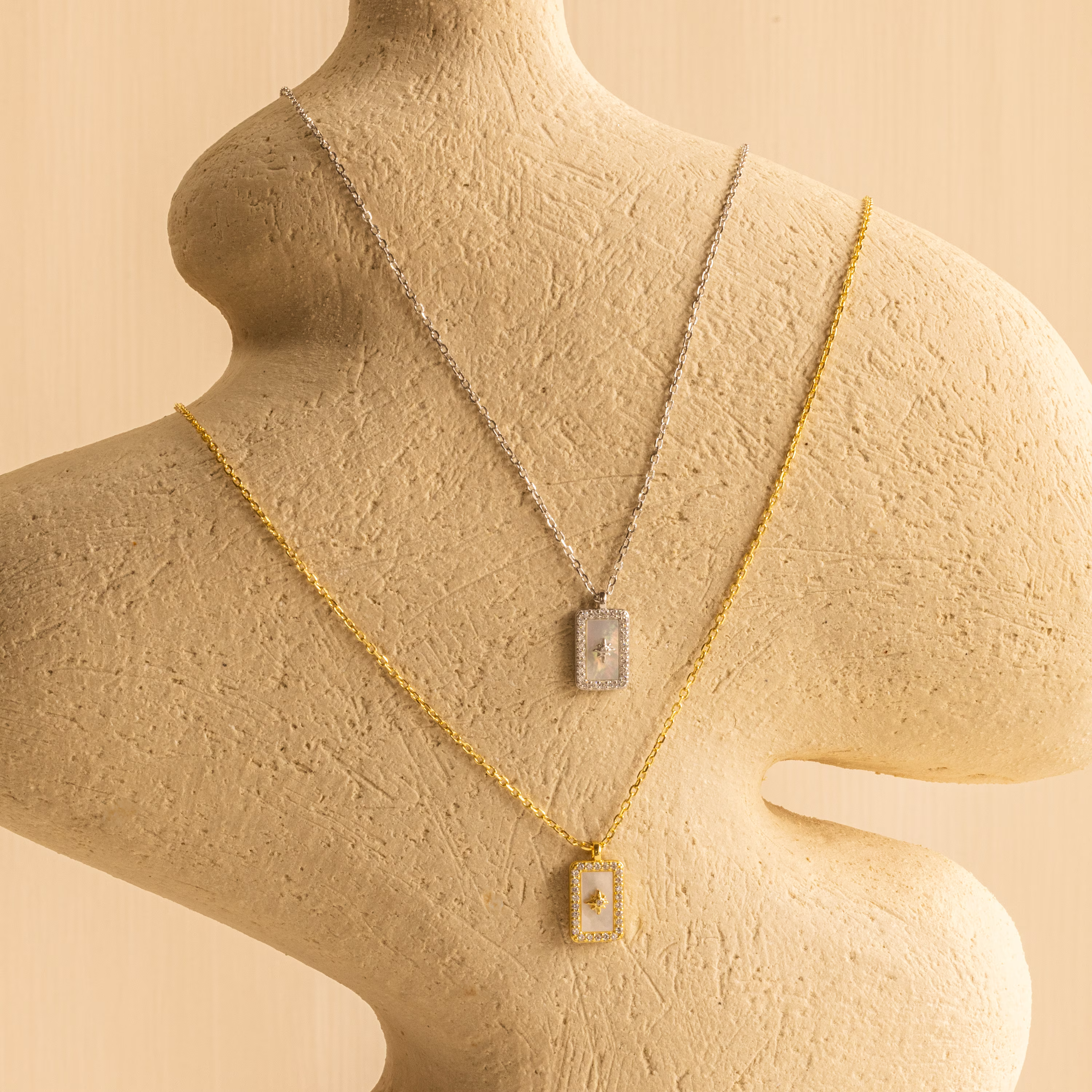 The Pave Pearl North Star Necklace adds celestial sparkle to a textured abstract beige mannequin, paired with a radiant gold Mother of Pearl pendant.
