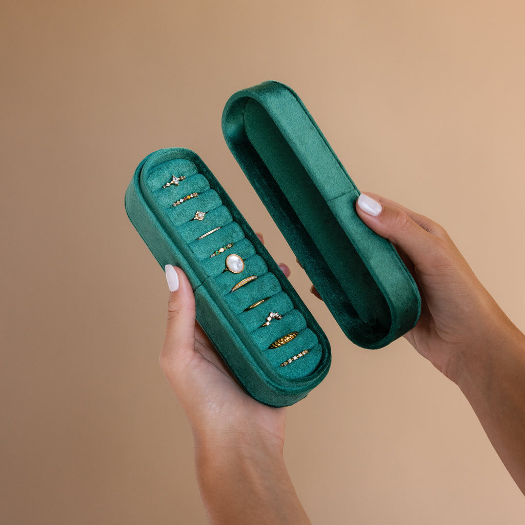 Hands holding an open Slim Velvet Ring Box on a beige background, showcasing multiple gold and gemstone rings—an elegant organizer and jewelry case for displaying your favorite pieces.