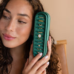 A woman smiles softly while holding the Slim Velvet Ring Box in green, displaying elegant gold rings.