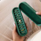 A person holds an open Slim Velvet Ring Box containing several gold rings with gems and pearls, highlighting its elegance as a ring organizer.