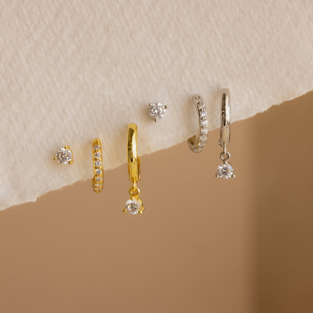 The Classic Diamond Earrings Set in Sterling Silver, featuring five elegant stud and hoop designs, is perfect for wedding jewelry and beautifully displayed on a textured cream surface.