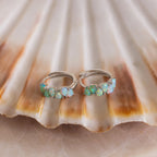 Ombre Opal Huggies—silver hoop earrings with small, iridescent opal stones displayed on a scallop shell—bring ocean-inspired elegance and luminous style to any look.