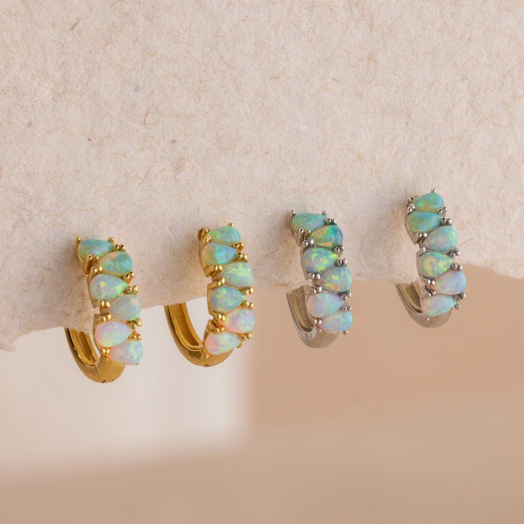 Four Ombre Opal Huggies earrings—featuring iridescent green opal stones in both gold and silver—are displayed on a textured surface.