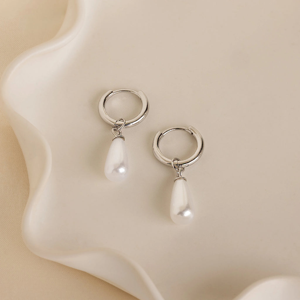 Pearl Teardrop Huggies—silver hoop earrings with dangling teardrop pearls, ideal as bridal hoop earrings—displayed on a wavy-edged white ceramic dish.