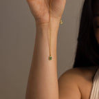 Someone displays the North Star Birthstone Necklace, featuring a gold finish and a small green crystal pendant, against a neutral background.