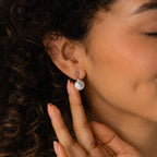 Smiling with her eyes closed, a woman with curly hair touches her Round Pearl Drop Earrings.