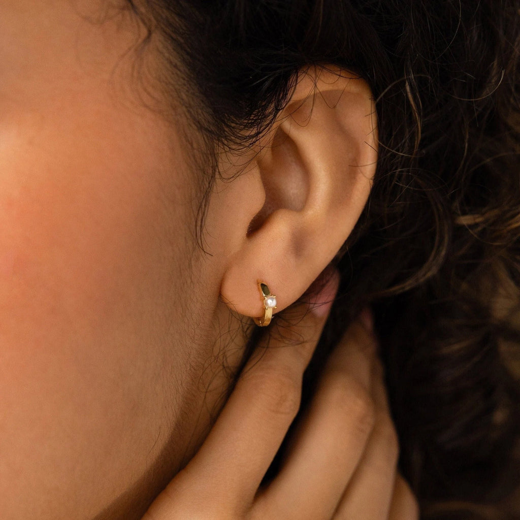 Close-up of a person’s ear wearing Tiny Pearl Huggies; hand rests gently on neck.