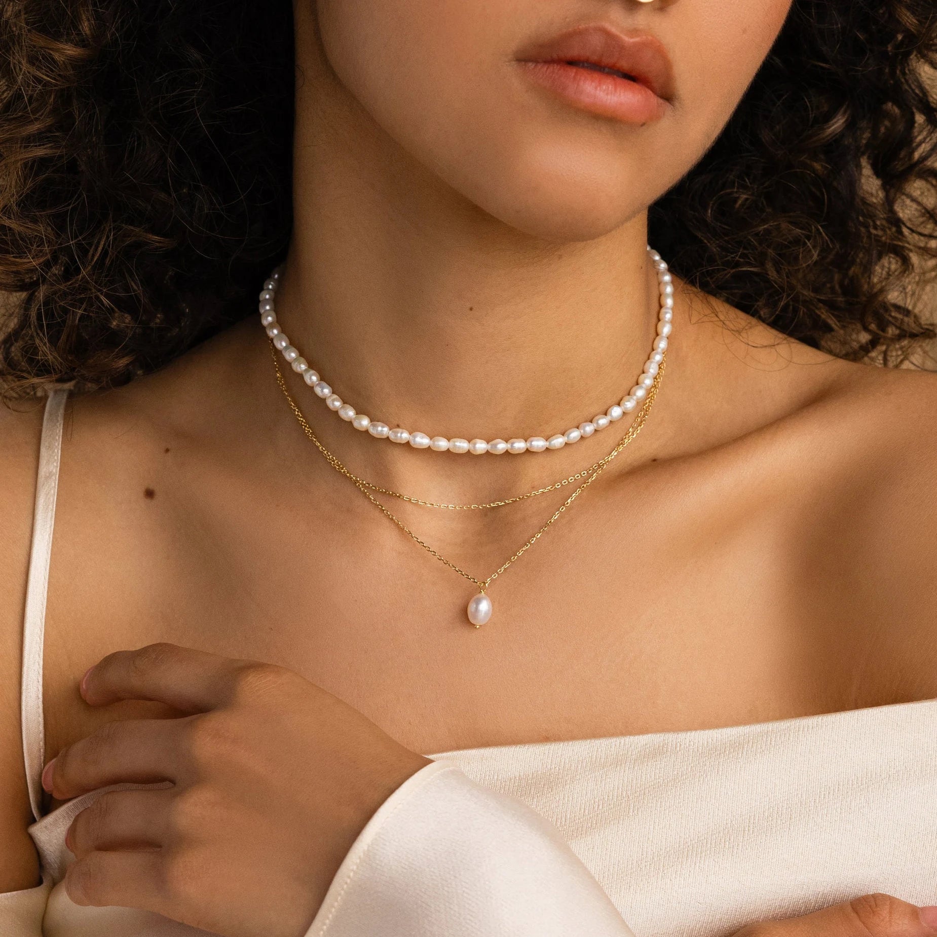 A woman elegantly layers the Duo Chain Pearl Necklace over an off-shoulder white top.