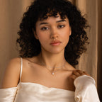 Woman with curly hair in an off-shoulder cream top showcases the Duo Chain Pearl Necklace, posing against a beige curtain backdrop.