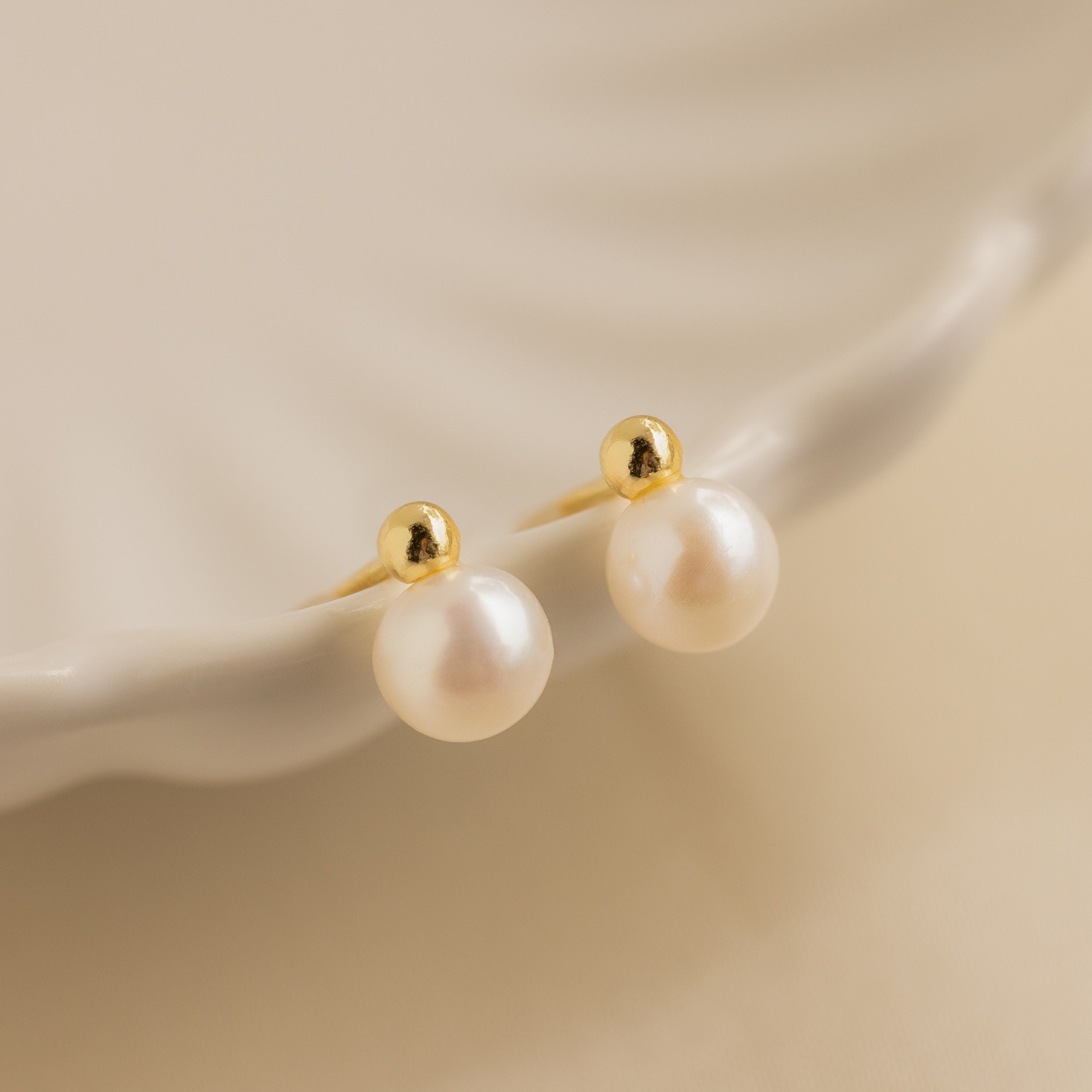 Classic Pearl Studs rest elegantly on the edge of a white, scalloped ceramic dish.