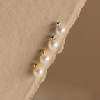 The Classic Pearl Studs are elegantly displayed on a textured beige fabric background, paired with gold and silver stud earrings for a timeless look.