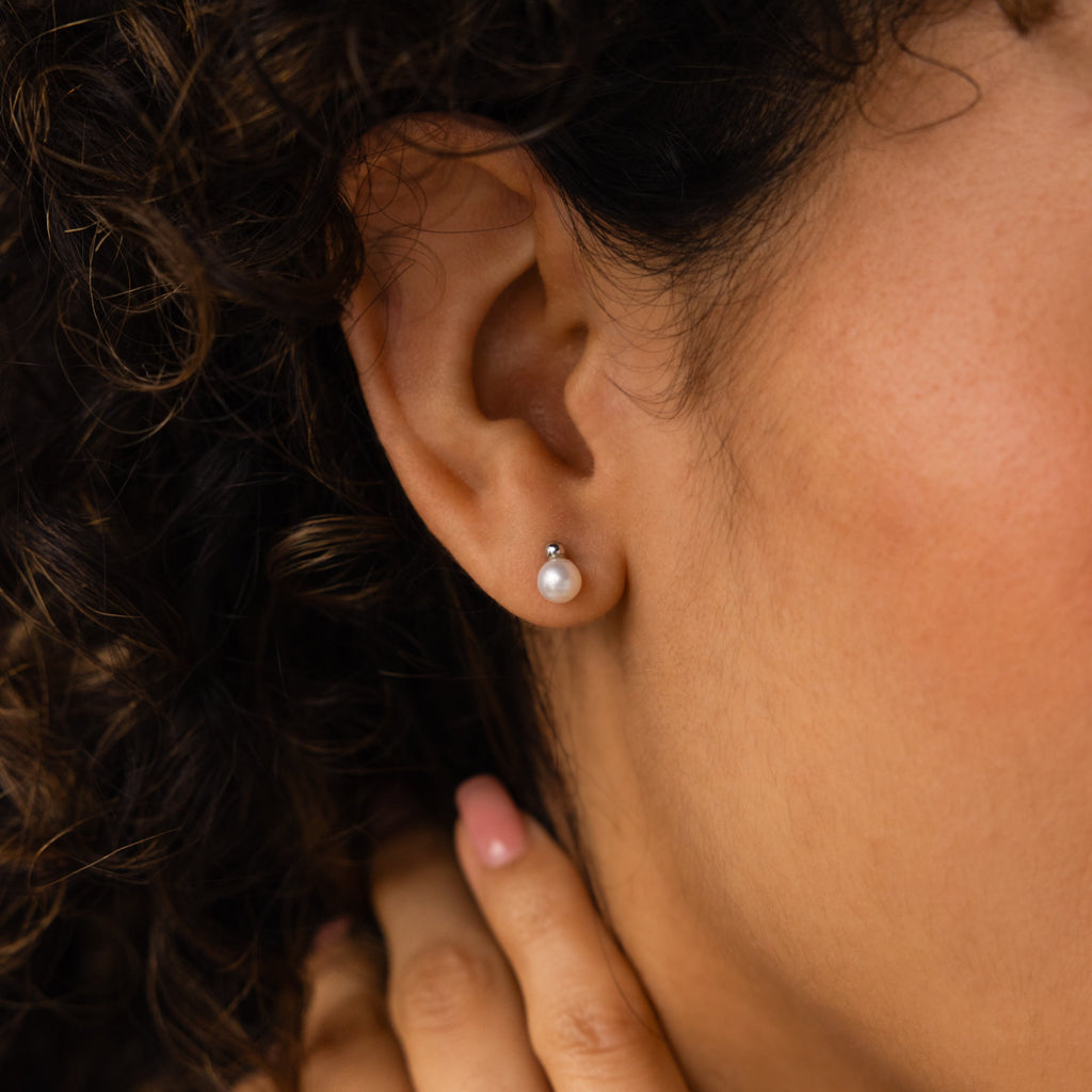 A close-up of a woman’s ear wearing Classic Pearl Studs, with her curly hair elegantly framing the timeless earrings.