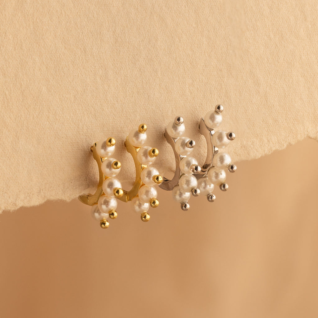 Beaded Pearl Huggies in gold and silver, adorned with pearls, displayed on a textured beige surface—ideal for lovers of modern pearl jewelry.