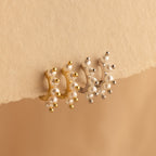 Beaded Pearl Huggies in gold and silver, adorned with pearls, displayed on a textured beige surface—ideal for lovers of modern pearl jewelry.