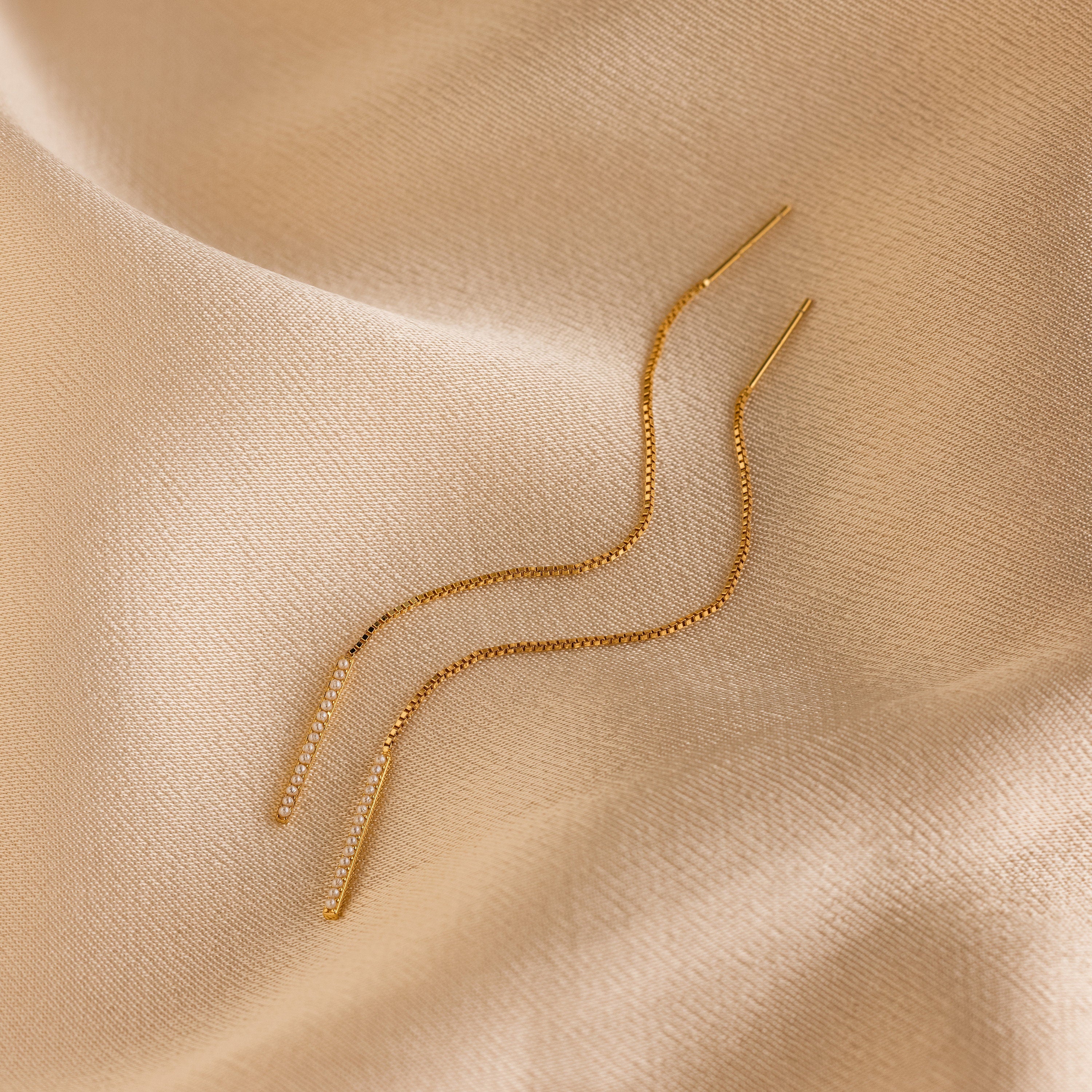Pearl Bar Threader Earrings displayed on smooth beige satin fabric, these dainty earrings bring modern elegance to any look—a must-have pearl jewelry essential.
