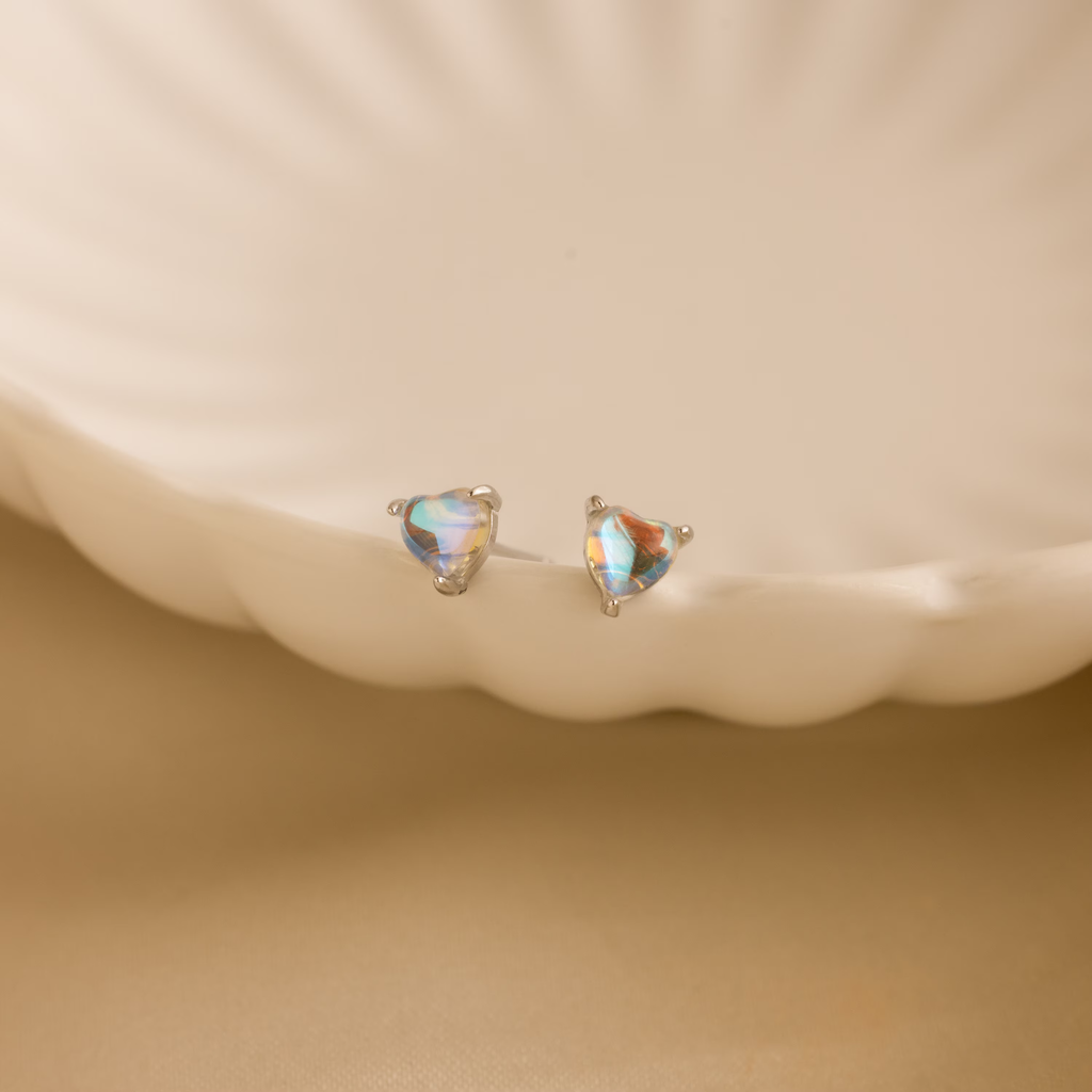 Moonstone Heart Studs displayed on a cream-colored, scalloped ceramic dish—ideal for those who love dainty earrings with a hint of elegance.