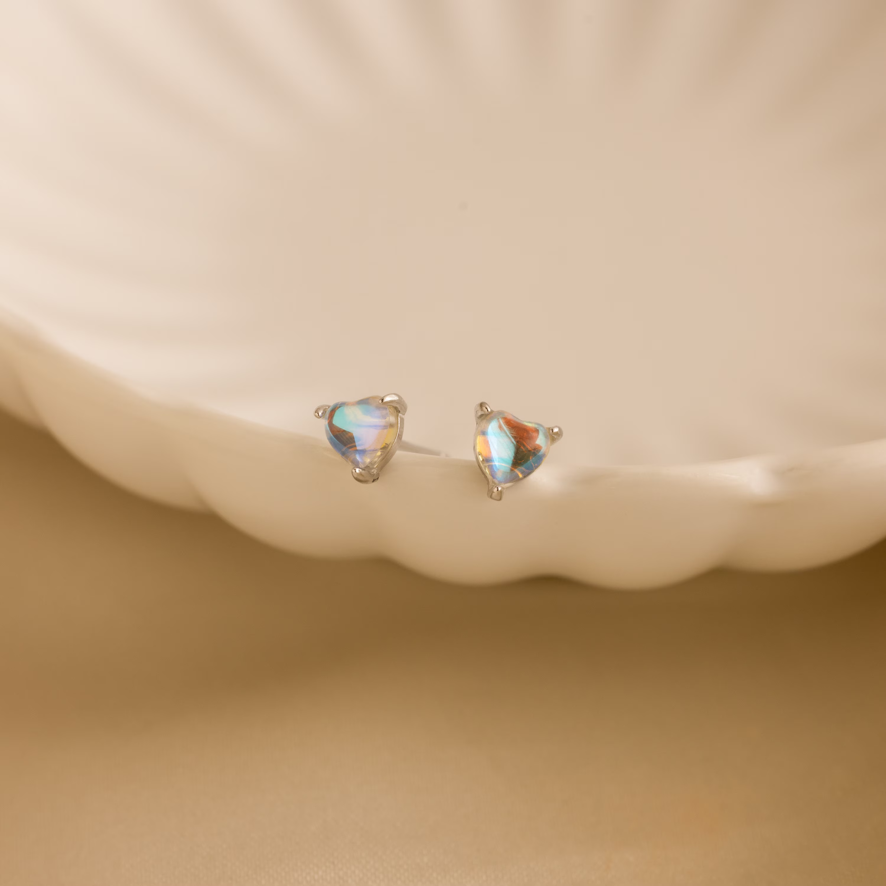Moonstone Heart Studs displayed on a cream-colored, scalloped ceramic dish—ideal for those who love dainty earrings with a hint of elegance.