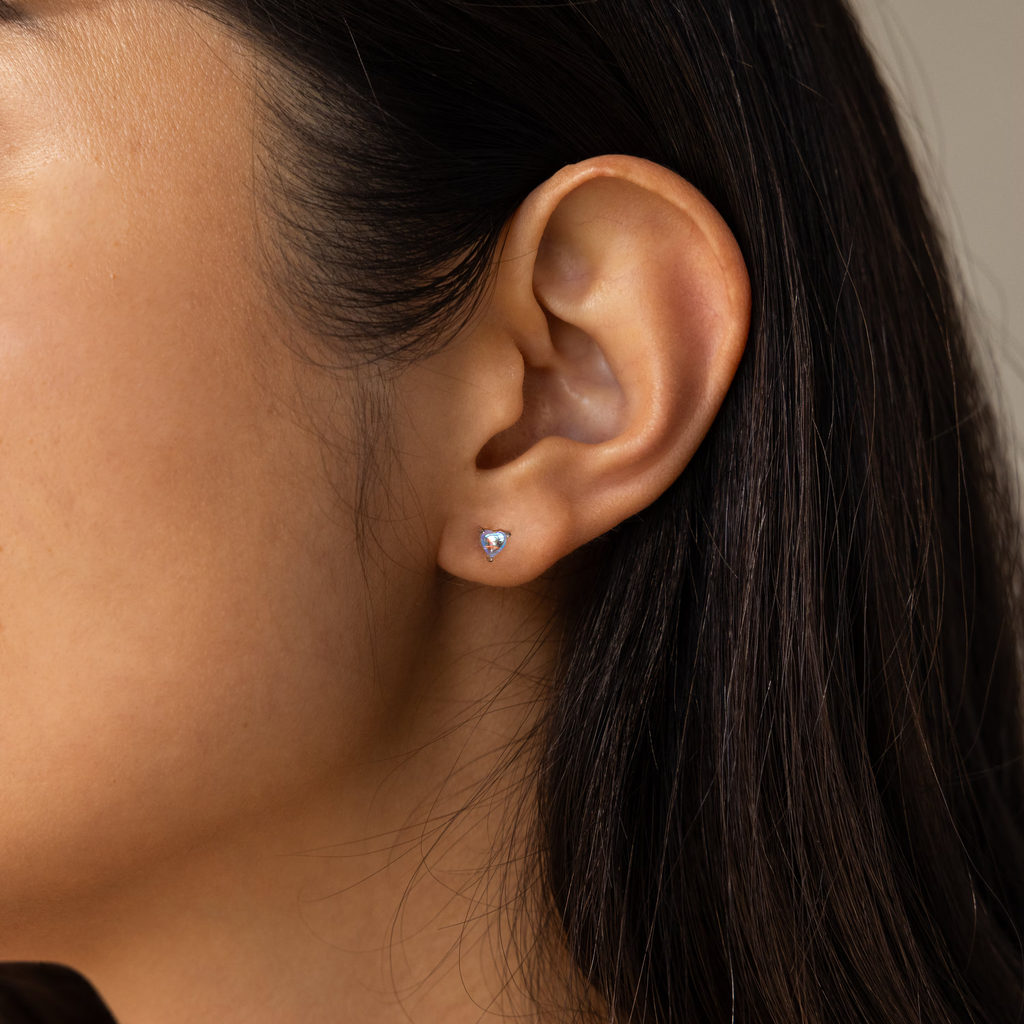 Close-up of a woman's ear wearing Moonstone Heart Studs—dainty earrings with small, heart-shaped moonstone and a clear gemstone accent.