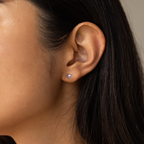 Close-up of a woman's ear wearing Moonstone Heart Studs—dainty earrings with small, heart-shaped moonstone and a clear gemstone accent.