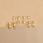 Six pairs of dainty earrings—featuring Moonstone Heart Studs plus star, round, and heart shapes—adorned with moonstone gems, displayed on a beige surface.