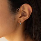 Close-up of a woman's ear wearing Moonstone Heart Huggies—delicate earrings with tiny, heart-shaped moonstones that shimmer softly in the light.