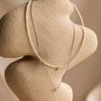 The Pearl & Diamond Duo Necklace is draped elegantly over a beige abstract sculpture.