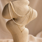 The Pearl & Diamond Duo Necklace is showcased on a textured beige jewelry stand against a neutral background.