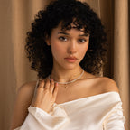 Woman with curly hair, in an off-shoulder white top, stands against a beige curtain wearing the Pearl & Diamond Duo Necklace.