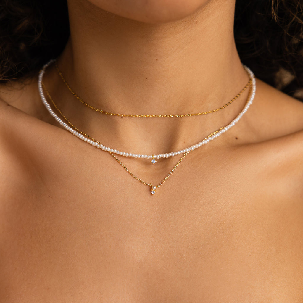 Close-up of a woman's neck showcasing the Pearl & Diamond Duo Necklace, elegantly layered with a pearl choker and gold chain featuring a diamond pendant.