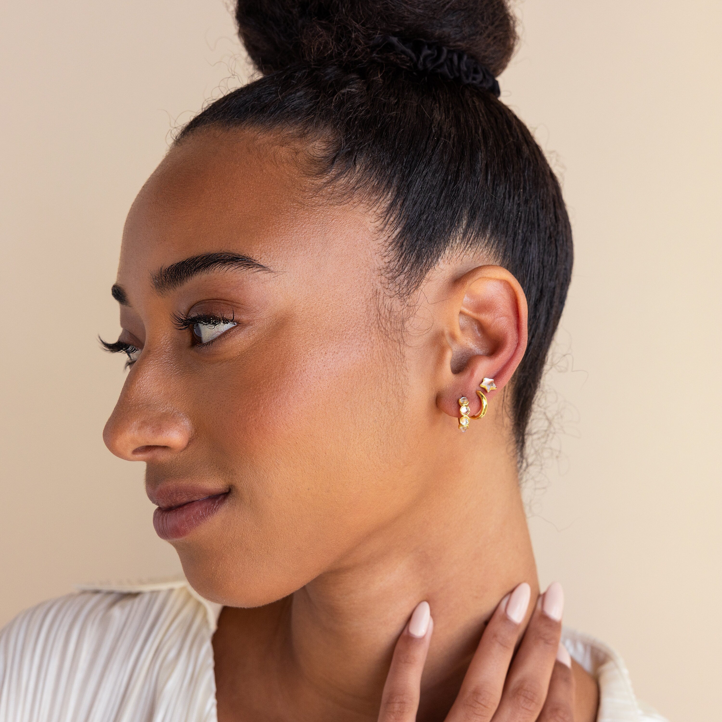 Woman with a bun hairstyle wears celestial Moonstone Star Studs, looking to the side and gently touching her neck.