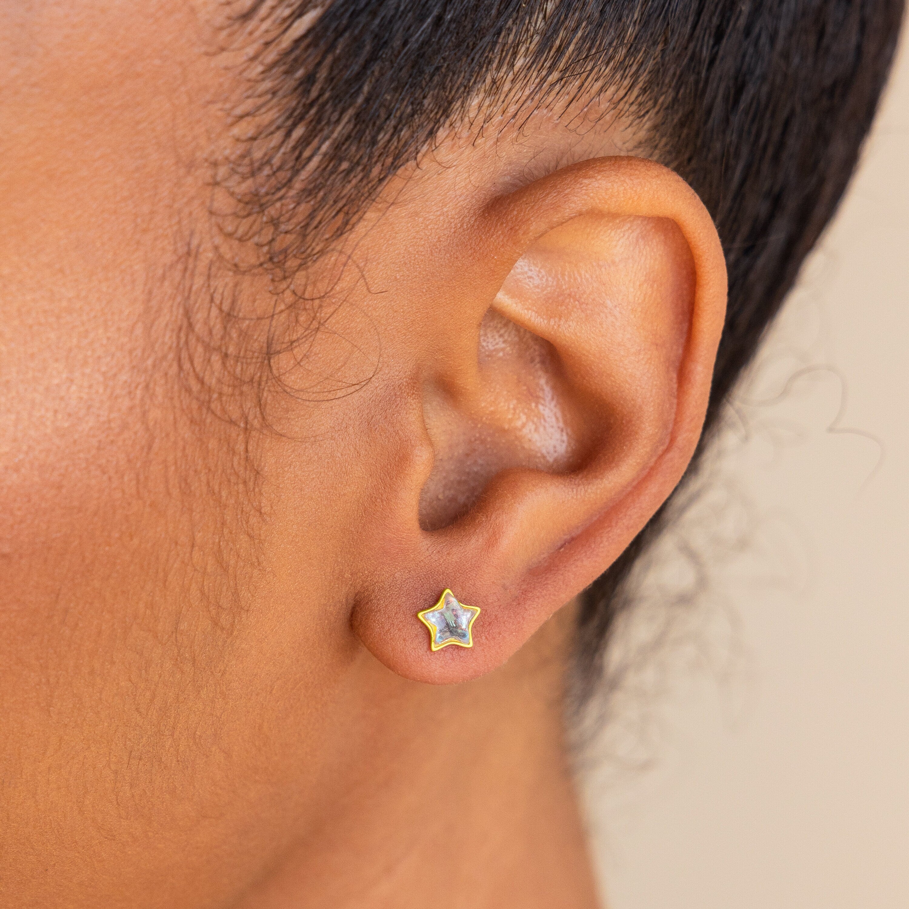 Close-up of a person’s ear wearing Moonstone Star Studs, small gold star-shaped earrings—an elegant choice for celestial jewelry lovers.